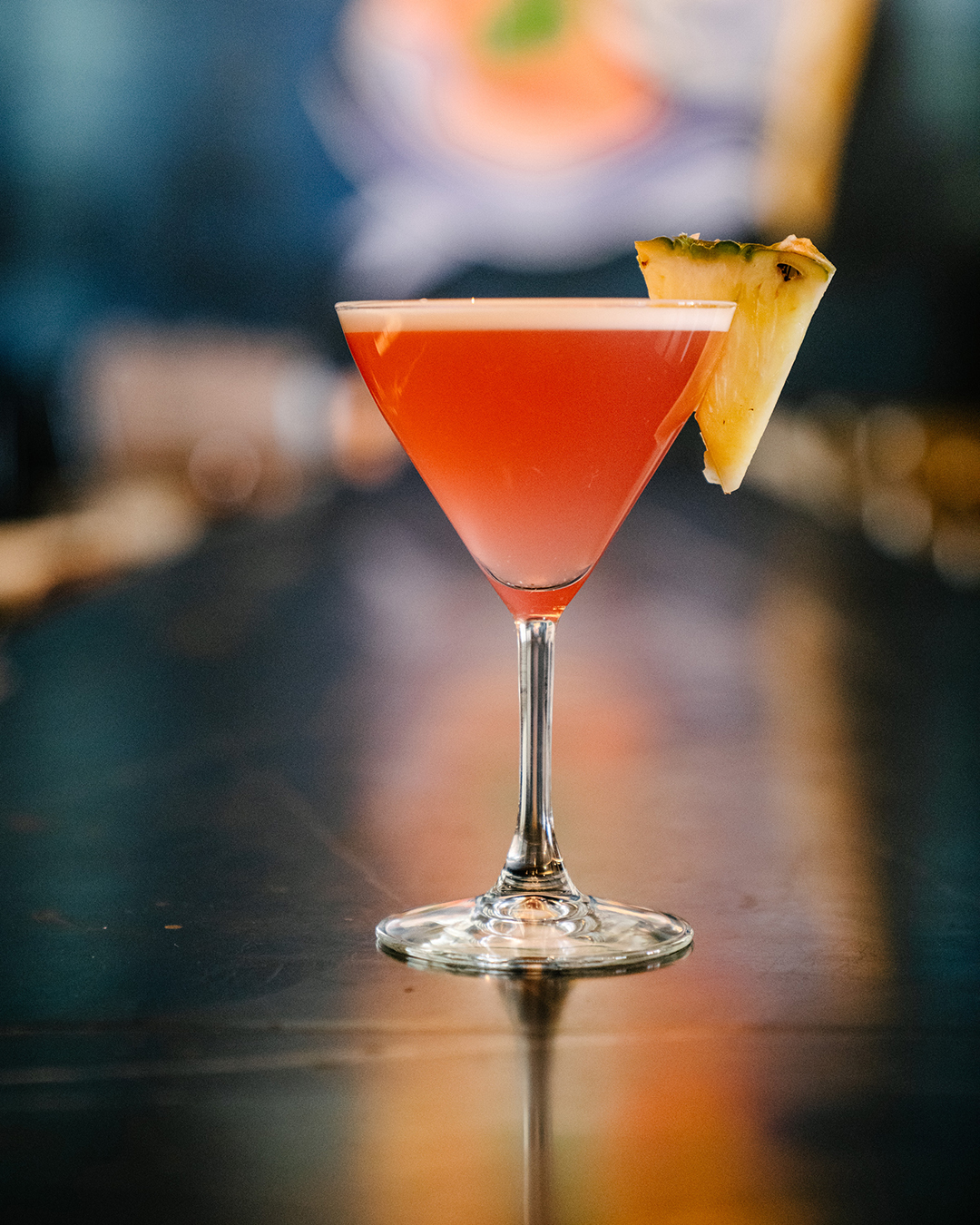A pink Amalfi cocktail in a stemmed glass with a pineapple garnish