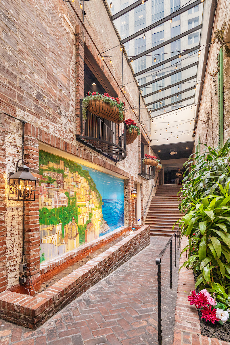 The brick-lined entrance to Amalfi with a coastal mural, flowers and string lights