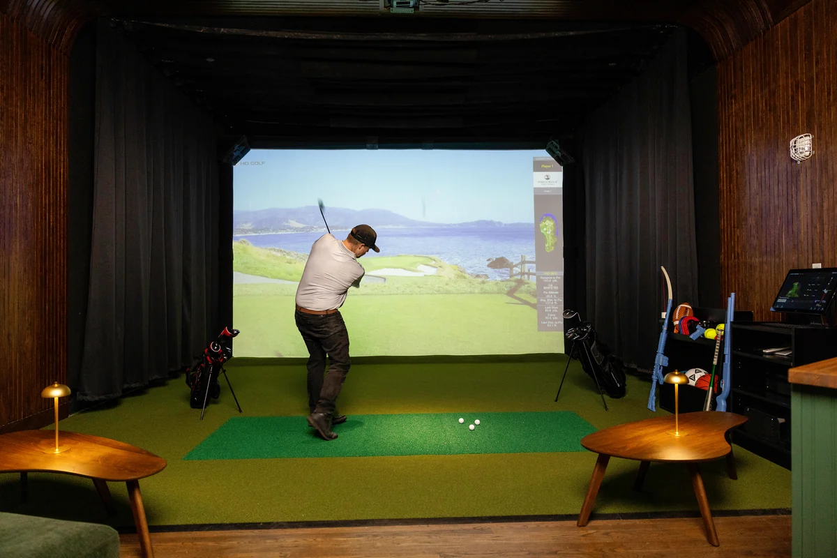A guest taking a golf swing in a Peachtree Sporting Club sports suite